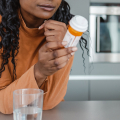 Mujer leyendo un frasco de medicina en una cocina con un vaso de agua cerca.
