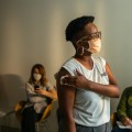 Woman holding an absorbent cotton to her arm after vaccination in a waiting room with other people seated in the background.