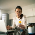 Una mujer frente a una computadora portátil mirando una botella de medicamento.