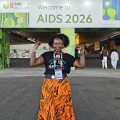 A Girl Like Me blogger Eliane (“HIVstigmafighter”) in front of AIDS 2026 sign.