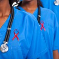 Close up of upper bodies of 3 medical professionals wearing red ribbons on their shirts.