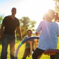 Man smiling at the park with two children on a see-saw.