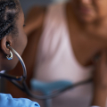 Health care professional using stethoscope to listen to woman's heart.