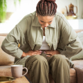 Woman sitting on a sofa, hunched over and holding her stomach in pain.