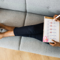 Woman on sofa circling dates on calendar.