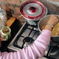 Woman in a kitchen, cookng at a stove.