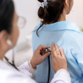 A healthcare professional holding a stethoscope on a woman's back.