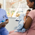 Woman holding baby talking to doctor in medical office.