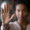 Woman with blurred face holding one hand in front of her, palm forward.