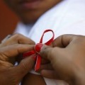 Hands pinning red ribbon to person's t-shirt sleeve.