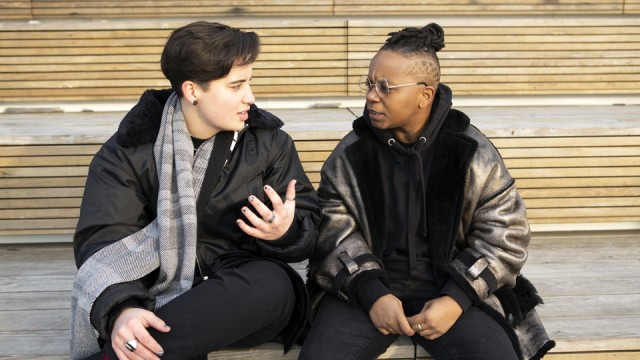 Two people sitting next to each other, outside, having a conversation.