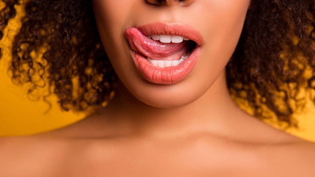 Close up of woman from bottom of nose to top of chest, her tongue licking her upper lip.