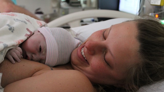 Heather O'Connor in hospital bed, smiling, holding newborn baby on her chest.