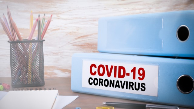 Pencil cup, pencils, notepad, and two binders on desk. One binder is labeled "COVID-19 Coronavirus".