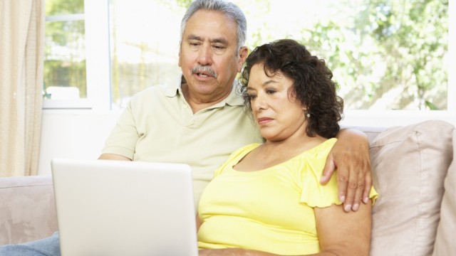Una pareja mayor sentada en un sofá mirando una laptop juntos.