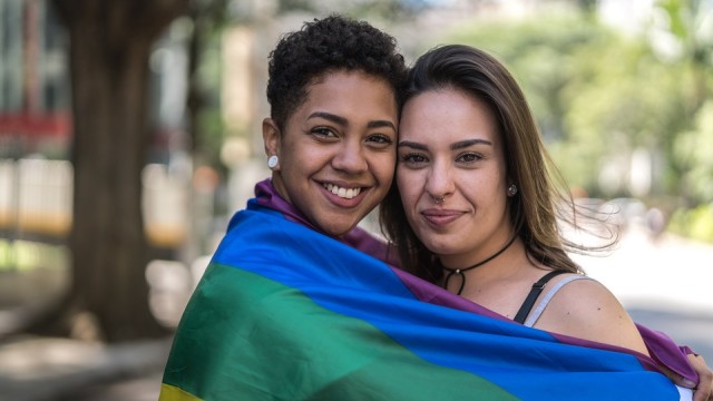 Two people smiling and hugging, wrapped in colorful flag.