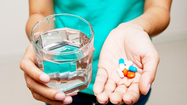 Manos de una persona sosteniendo pastillas en una y un vaso de agua en la otra.