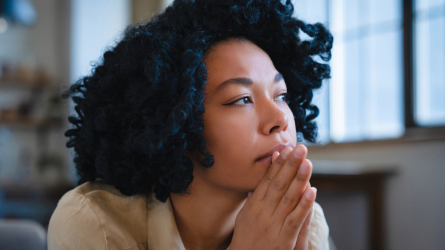 Woman with hands together in front of chin looking up and to the side.