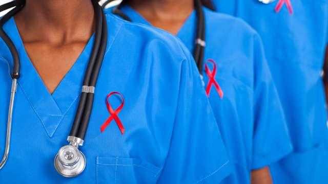 Close up of upper bodies of 3 medical professionals wearing red ribbons on their shirts.