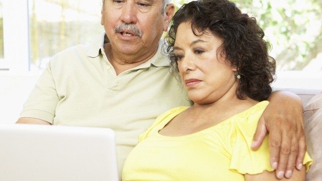 Una pareja mayor sentada en un sofá mirando una laptop juntos.