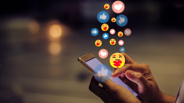 Woman using a smartphone on social media with emoji reactions floating out of phone.