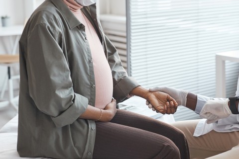 Pregnant woman sitting on examination table getting pulse taken. 