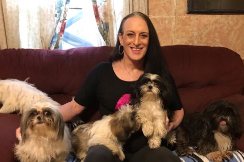 Katie Willingham, smiling, sitting on sofa with five small dogs.