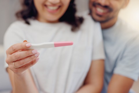 Una pareja, sonriendo, mirando los resultados de una prueba de embarazo casera.
