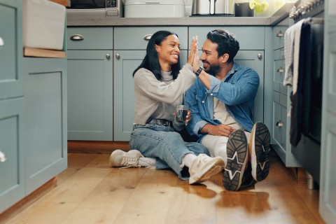 Una pareja sentada en el suelo de la cocina chocando los cinco.