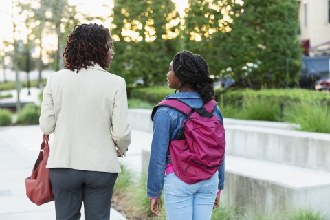 Woman and girl walking on a sidewalk talking. 