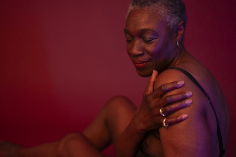 Woman with eyes closed, her hand touching her shoulder.