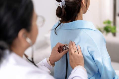 A healthcare professional holding a stethoscope on a woman's back.
