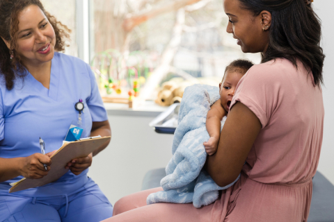 Woman holding baby talking to doctor in medical office.