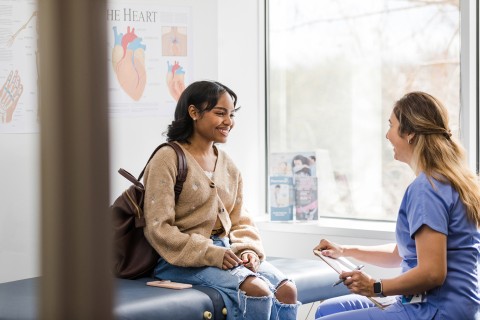 Mujer y profesional de la salud sonriendo y hablando en el consultorio médico.