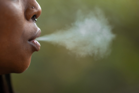 Profile of face of woman blowing smoke out of her mouth.