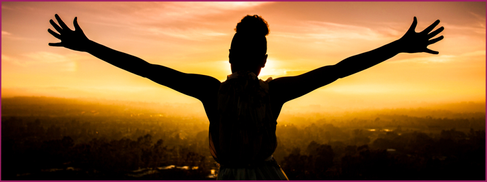 Silhouette of woman with arms outstretched looking over valley.