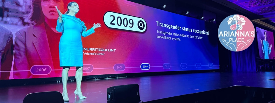 Arianna Lint standing on stage with presentation on screen behind her.