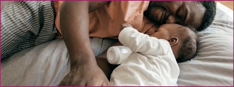 Parent and baby with bottle on a bed.