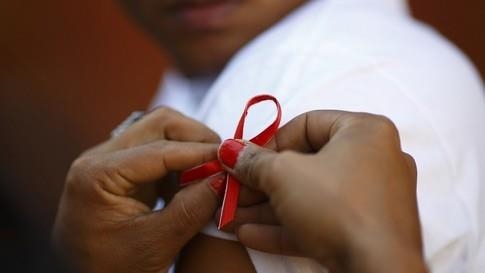 Hands pinning red ribbon to person's t-shirt sleeve.