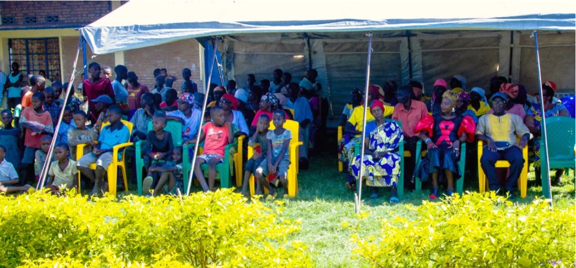 Many people sitting in chairs outside under a covering.