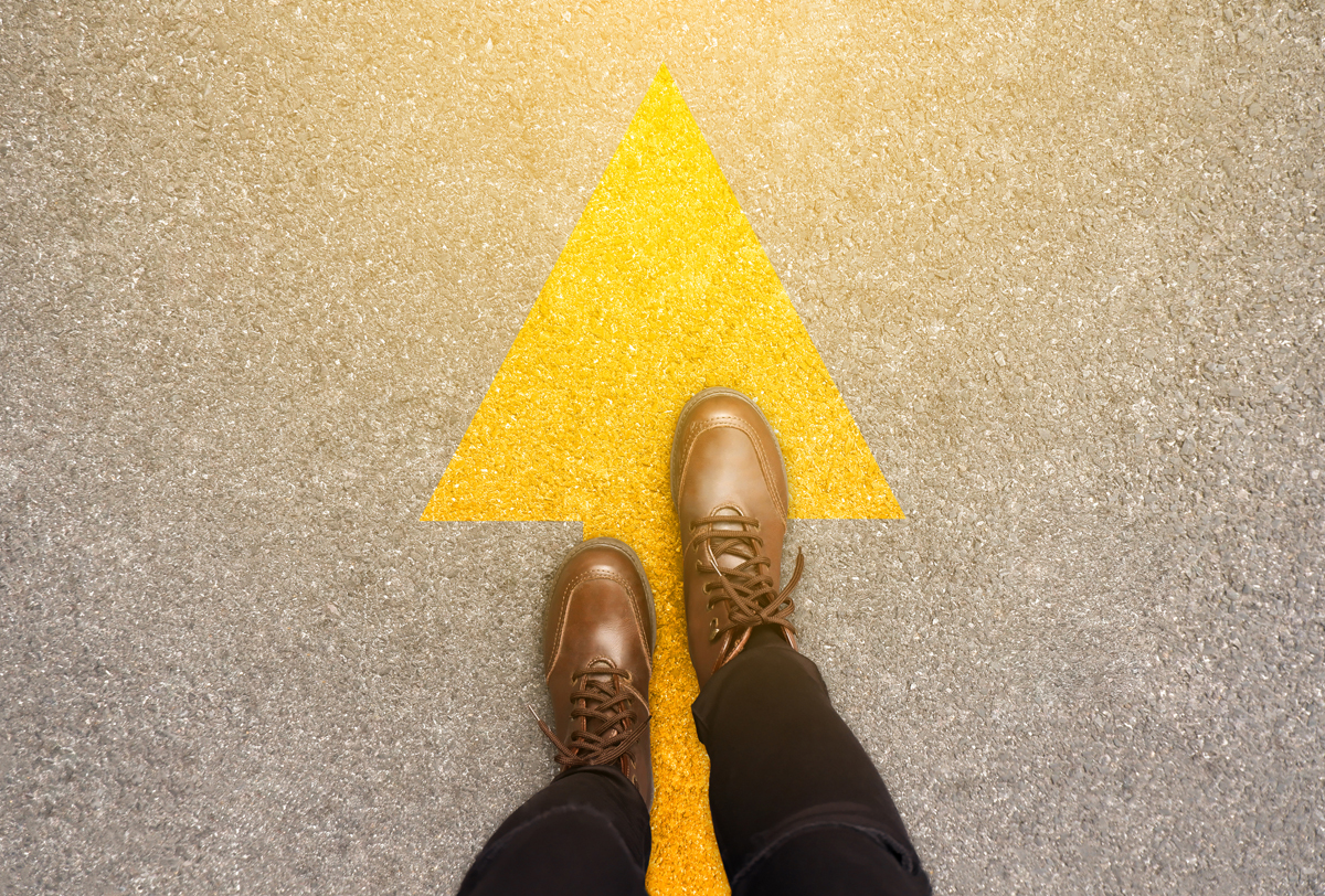 Close up of feet in shoes on walking forward on yellow arrow.